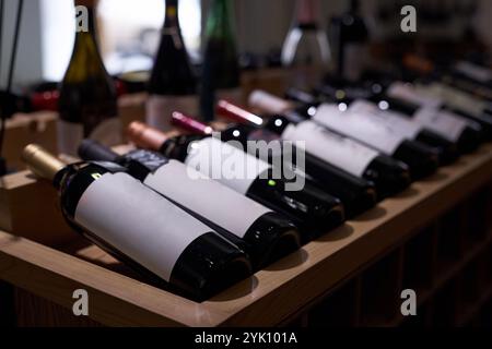 Mittlere Nahaufnahme von schwach beleuchteten Flaschen mit gereiftem Rotwein auf Holztisch während der Präsentation Stockfoto