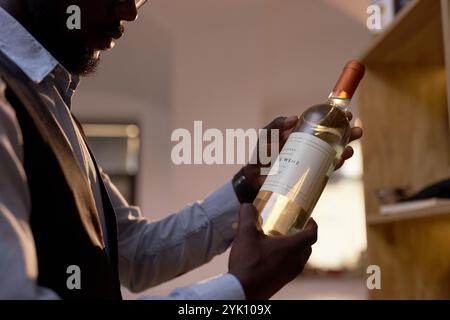 Mittlere Nahaufnahme einer Kristallflasche mit teurem Wein in nicht erkennbaren afroamerikanischen Händen Stockfoto