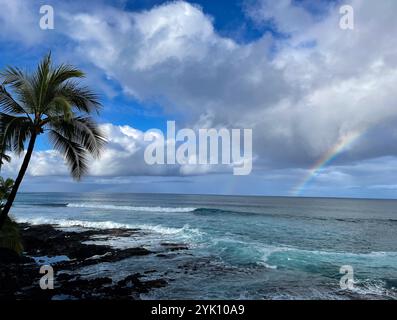 Vor der Küste von Kailua Kona auf der Big Island von Hawaii erstreckt sich ein Regenbogen vom Horizont des Ozeans bis in die Wolken. Palmen schwingen Stockfoto