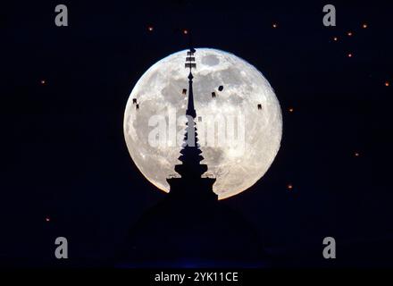 Der Vollmond erhebt sich hinter dem Buddha’s Footprint von Yonok City, begleitet von schwimmenden Lannas-Laternen am Loy Krathong Day im Wat Phra That Doi Saket. Stockfoto