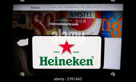 In dieser Abbildung hält eine Person ein Handy mit dem Logo der niederländischen Brauerei Heineken N.V. vor der Webseite. Stockfoto