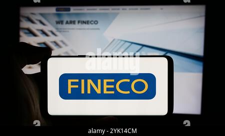 In dieser Abbildung hält eine Person ein Mobiltelefon mit dem Logo des italienischen Finanzdienstleisters FinecoBank S.p.A. vor der Webseite. Stockfoto