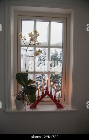 Winterfenster mit Schnee auf der Außenseite und Adventskerzenleuchter und Blume auf der Innenseite Stockfoto