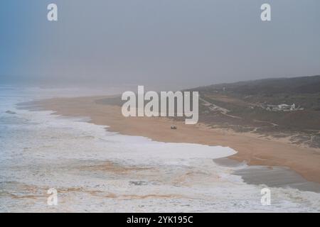 Ein großer Blick auf einen leeren Küstenstrand mit sanften Wellen, Sandstränden und nebeligem Himmel im Hintergrund Stockfoto