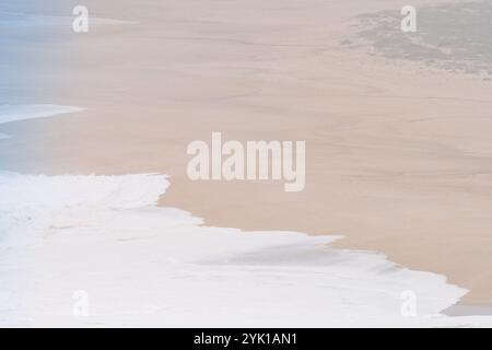 Weiche weiße Wellen brechen sanft auf einen riesigen Sandstrand in Nazare, Portugal Stockfoto