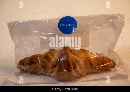 Ein frisch gebackenes Croissant, verpackt in einer durchsichtigen Tüte von Greggs, auf einem hellen Hintergrund, der seine blättrige Textur zeigt Stockfoto