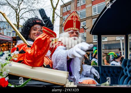 Nikolaus und seine Helferin begrüßen das Publikum. Am ersten Samstag nach dem 11. November trifft die rot-weiß-bekleidete Sinterklaas (St. Nikolaus) in mehreren niederländischen Städten ein. In Nijmegen ging Sinterklaas auf einer Route durch das Stadtzentrum, begleitet von seinen Helfern, dem Pieten (Peters), der Kindern und Erwachsenen traditionelle Süßigkeiten schenkte. Stockfoto