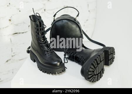 Schwarze Lederstiefel für Damen und ein schwarzer Lederrucksack stehen auf weißem Hintergrund. Damenmode Stockfoto