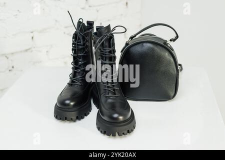 Schwarze Lederstiefel für Damen und ein schwarzer Lederrucksack stehen auf weißem Hintergrund. Damenmode Stockfoto