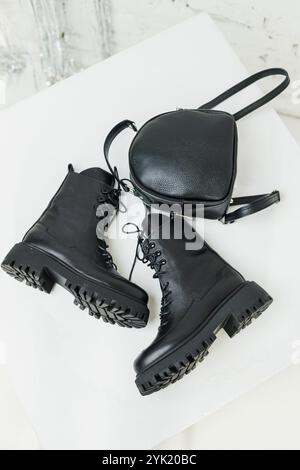 Schwarze Lederstiefel für Damen und ein schwarzer Lederrucksack stehen auf weißem Hintergrund. Damenmode Stockfoto