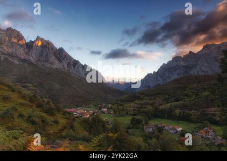 Vormittagsblick auf das Bergdorf Posada de Valdeon. Berggipfel, die von der Sonne beleuchtet werden. Farne im Vordergrund. Stockfoto