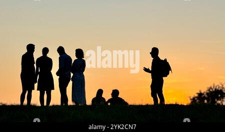 Silhouette einer Gruppe von Menschen bei Sonnenuntergang im Olympiapark München im Juli 2024 Stockfoto