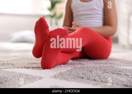 Kind in roten Strumpfhosen sitzt zu Hause auf dem Boden, Nahaufnahme Stockfoto