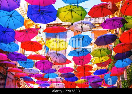 Bunte Regenschirme hängen in der Luft über einer engen Straße. Regenschirme sind in Blau-, Rot-, Rosa-, Lila- und Gelbtönen gehalten. erzeugen eines Haubeneffekts Stockfoto