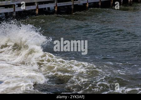 Wellen, die an einem bewölkten Tag am Meer gegen den Pier krachen, schaffen eine dynamische und lebhafte Atmosphäre am Ufer des Wassers Stockfoto