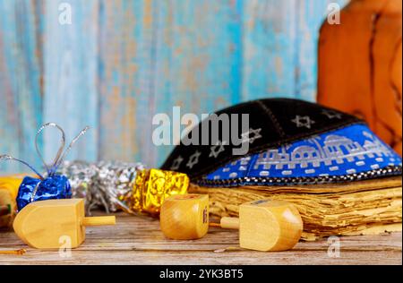 Farbenfrohe Dreidels-Schokoladengel ruhen auf Holztisch, begleitet von traditioneller Kippah, die festliche Atmosphäre für Chanukkah-Feiern schaffen. Stockfoto