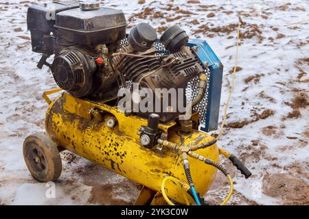 Der tragbare Luftkompressor befindet sich auf der Baustelle im Schlamm, wobei Schmutz um die Geräte verteilt ist, was auf aktive Arbeiten hinweist. Stockfoto