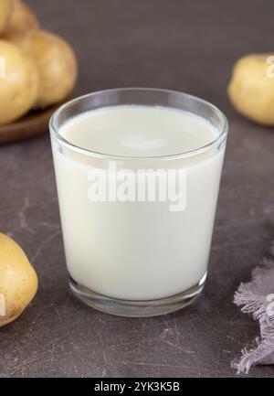 Vegane Kartoffelmilch und Kartoffeln auf braunem Hintergrund. Pflanzliche laktosefreie Milch. Gemüsemilch. Stockfoto