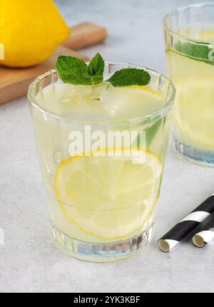Limonade mit Zitronen-, Minz- und Eiswürfeln in Glas auf grauem Hintergrund. Kaltes Sommergetränk. Stockfoto