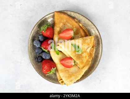 Französische Crepes, Pfannkuchen oder russische Bliny mit Erdbeeren, Heidelbeeren und Minze auf grauem Hintergrund. Draufsicht. Stockfoto