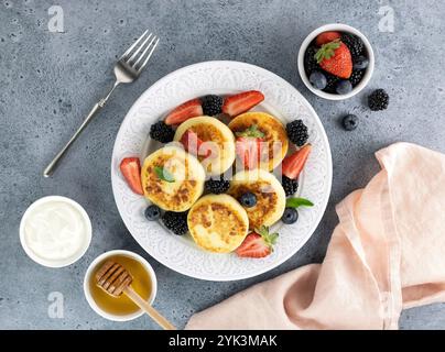 Hüttenkäsepfannkuchen, Syrniki mit Sauerrahm, Honig, Beeren auf blauem Hintergrund. Draufsicht. Russisches, ukrainisches Essen Stockfoto