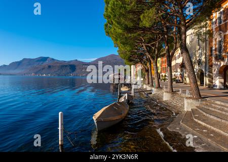 Alte schöne Stadt mit Gebäude und Bäumen an der Uferpromenade am Luganer See mit Boot an einem sonnigen Tag mit Berg in Morcote, Tessin, Schweiz. Stockfoto