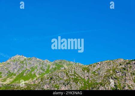 Wunderschönes Haus und Kommunikationsturm auf der Bergkette gegen den blauen Himmel an einem sonnigen Sommertag in Andermatt, URI, Schweiz. Stockfoto