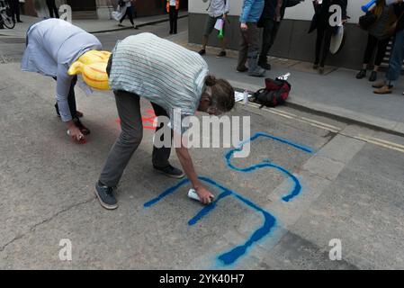 London, Großbritannien. Juni 2017. Zwei Leute sprühen einen Kreide-Sprugans auf die Straße, während andere abwechselnd „London School of Exploitation“ mit lautem Vuvuzelas singen. Die LSE Street Theatre Proteste für Life Not Money wurden zur Unterstützung von Reinigungskräften der London School of Economics eingesetzt, die wöchentlich für Gleichstellung streikten. Die LSE und die Arbeitgeber Noonan behandeln sie als Bürger zweiter Klasse, die sich weigern, ihre gewerkschaft die Vereinigten Stimmen der Welt anzuerkennen und ihnen eine niedrige Bezahlung und grob minderwertige Bedingungen für direkt beschäftigte Mitarbeiter zu gewähren. Stockfoto