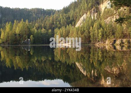 see zwischen Felsen und Wäldern zur goldenen Stunde. Wälder spiegeln sich auf der Wasseroberfläche wider Stockfoto