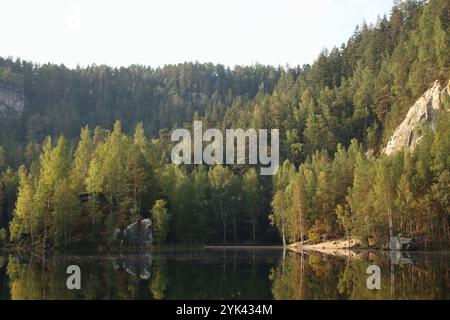 see zwischen Felsen und Wäldern zur goldenen Stunde. Wälder spiegeln sich auf der Wasseroberfläche wider Stockfoto