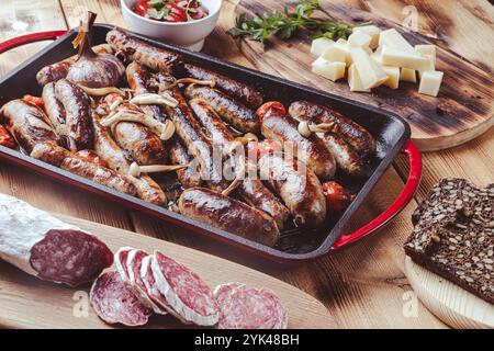 Grillpfanne mit leckeren hausgemachten Hühnchen-, Rind- und Schweinefleisch-Würstchen, Pilzen und Tomaten auf einem Holztisch mit Ketchup, Brot und Käse. Hoch Stockfoto