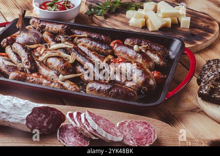 Grillpfanne mit leckeren hausgemachten Hühnchen-, Rind- und Schweinefleisch-Würstchen, Pilzen und Tomaten auf einem Holztisch mit Ketchup, Brot und Käse. Hoch Stockfoto