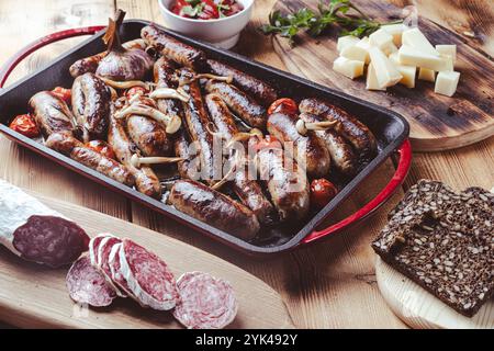 Grillpfanne mit leckeren hausgemachten Hühnchen-, Rind- und Schweinefleisch-Würstchen, Pilzen und Tomaten auf einem Holztisch mit Ketchup, Brot und Käse. Hoch Stockfoto