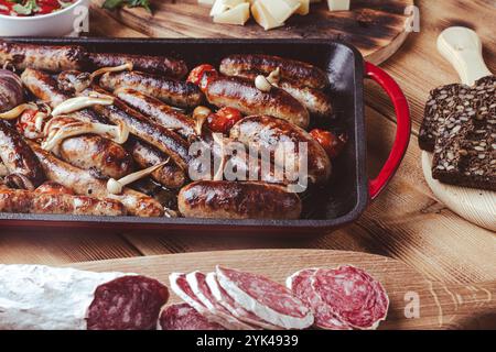 Grillpfanne mit leckeren hausgemachten Hühnchen-, Rind- und Schweinefleisch-Würstchen, Pilzen und Tomaten auf einem Holztisch mit Ketchup, Brot und Käse. Hoch Stockfoto