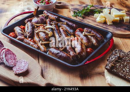Grillpfanne mit leckeren hausgemachten Hühnchen-, Rind- und Schweinefleisch-Würstchen, Pilzen und Tomaten auf einem Holztisch mit Ketchup, Brot und Käse. Hoch Stockfoto