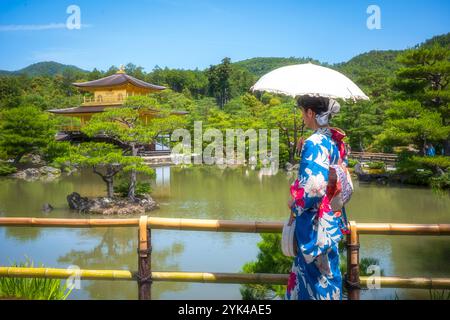 Kyoto, Japan - 19. Juni 2024: Eine Frau mit einem Regenschirm und einem traditionellen Kimono mit Flora blickt auf den Kinkakuji (Goldenen Pavillon), einen Tempelbau Stockfoto