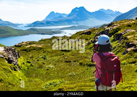 Ein Mädchen macht eine Wanderung in Lofoten, um die atemberaubende Aussicht auf Fjorde und Berge zu genießen und die atemberaubende nordische Landschaft zu betonen Stockfoto