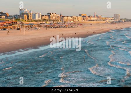 Menschen, die am öffentlichen Strand in Scheveningen spazieren gehen. Menschen, die beim Sonnenuntergang am öffentlichen Strand in Scheveningen spazieren gehen. Hotels und Wohngebäude im Hintergrund. Wellen des Norht-Meeres im Vordergrund. niederlande die hauge B97A7412 Stockfoto