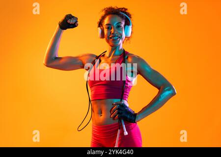 Sportliche schwarze hispanische Frau, die Sportswear trägt, Training im Fitnessstudio, farbenfrohe dramatische Beleuchtung - afroamerikanische Sportlerin, die Sport treibt Stockfoto