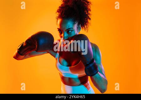 Sportliche schwarze hispanische Frau, die Sportswear trägt, Training im Fitnessstudio, farbenfrohe dramatische Beleuchtung - afroamerikanische Sportlerin, die Sport treibt Stockfoto