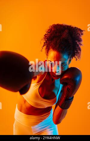 Sportliche schwarze hispanische Frau, die Sportswear trägt, Training im Fitnessstudio, farbenfrohe dramatische Beleuchtung - afroamerikanische Sportlerin, die Sport treibt Stockfoto