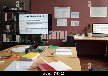 Geräumiger Schulungsraum mit interaktivem Brett mit Grammatikregeln, Plakaten an den Wänden und breitem Tisch mit Copybooks, Stiften und Testpapieren Stockfoto