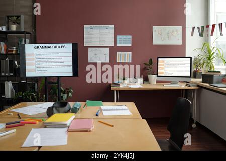 Interaktive Tafel mit Grammatikregeln, Plakaten an Wänden und breitem Tisch mit Copybooks, Stiften und Testpapieren im geräumigen Klassenzimmer Stockfoto