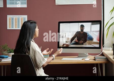 Junge Lehrerin mit Computerbildschirm im Klassenzimmer der modernen Sprachschule während des Online-Unterrichts mit männlichen Schülern Stockfoto