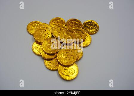 Schöne große Goldmünzen, Cent mit einem Dollarzeichen stehen auf einem weißen Plastikhintergrund. Geldbonbons, ein Schokoladenriegel in einem goldenen Metall. Stockfoto