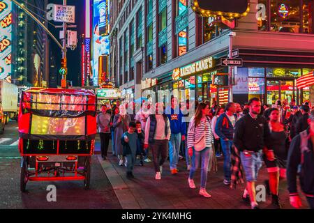 Bunte Nachtszene am Times Square mit beleuchtetem Pedicab und Menschenmenge, die an beleuchteten Ladenfronten vorbeiläuft. New York. USA. Stockfoto