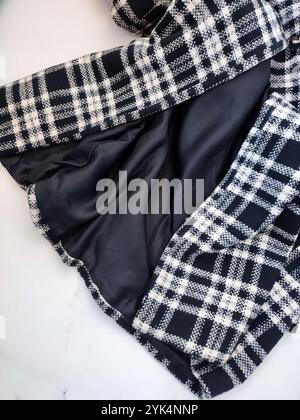 Gefütterter Mantel unten, schwarz weiß karierter Mantel mit satiniertem schwarzem Futter, Stoff, Textil, Kleidungsdetails, flach auf weißem Marmorhintergrund Stockfoto