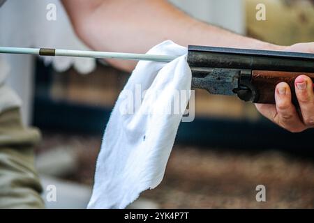 Ein Mann reinigt ein altes Gewehr sorgfältig mit Öl und Reinigungsgeräten und zeigt die Liebe zum Detail und die Handwerkskunst alter Schusswaffen. Stockfoto