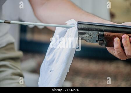 Ein Mann reinigt ein altes Gewehr sorgfältig mit Öl und Reinigungsgeräten und zeigt die Liebe zum Detail und die Handwerkskunst alter Schusswaffen. Stockfoto