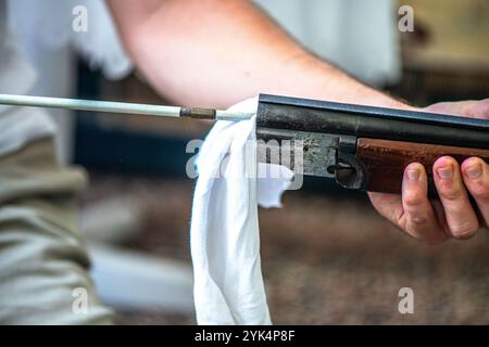 Ein Mann reinigt ein altes Gewehr sorgfältig mit Öl und Reinigungsgeräten und zeigt die Liebe zum Detail und die Handwerkskunst alter Schusswaffen. Stockfoto